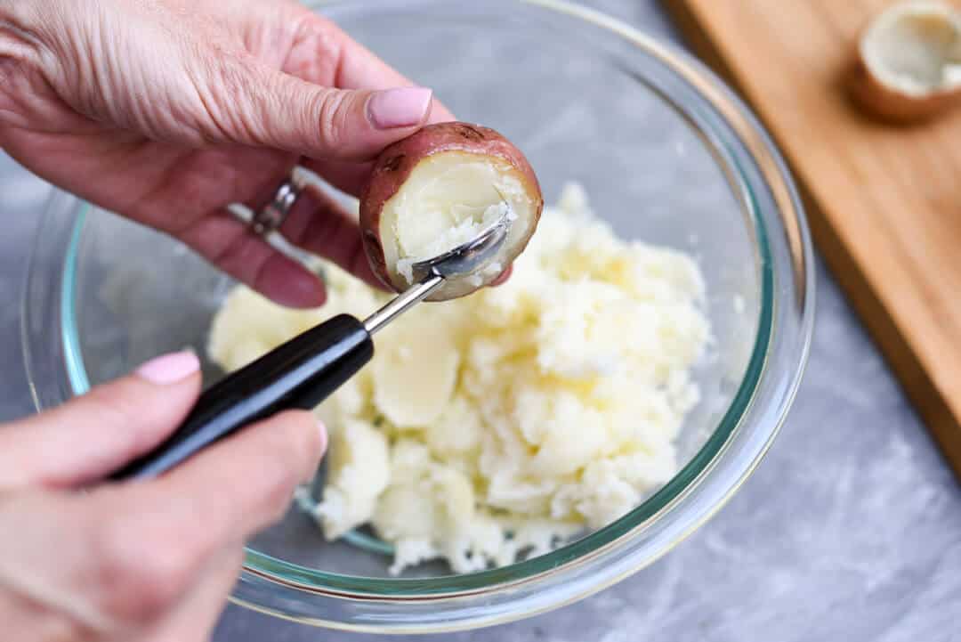 Using a melon baller to scoop the potato from the skin.