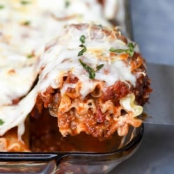 A spatula lifts a lasagna rollup from a baking dish.