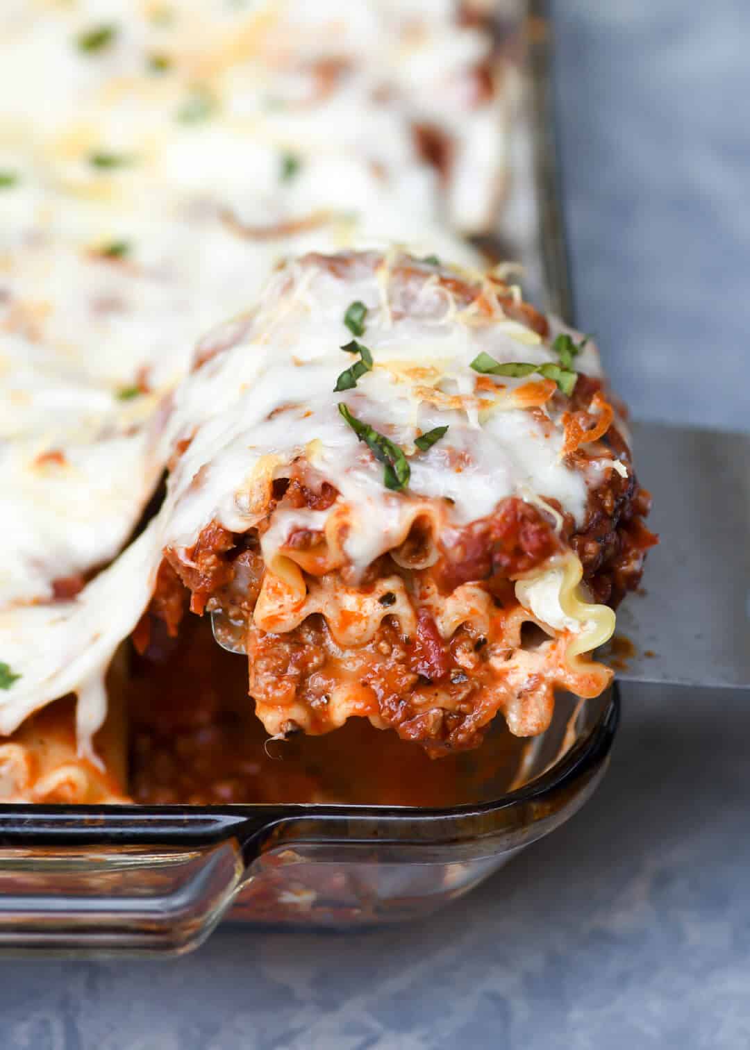 A spatula lifts a lasagna rollup from a baking dish.