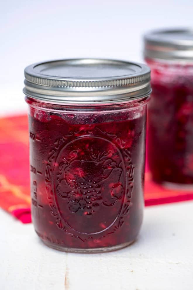 Very Berry Cranberry Sauce in a mason jar with a red cloth in the background.