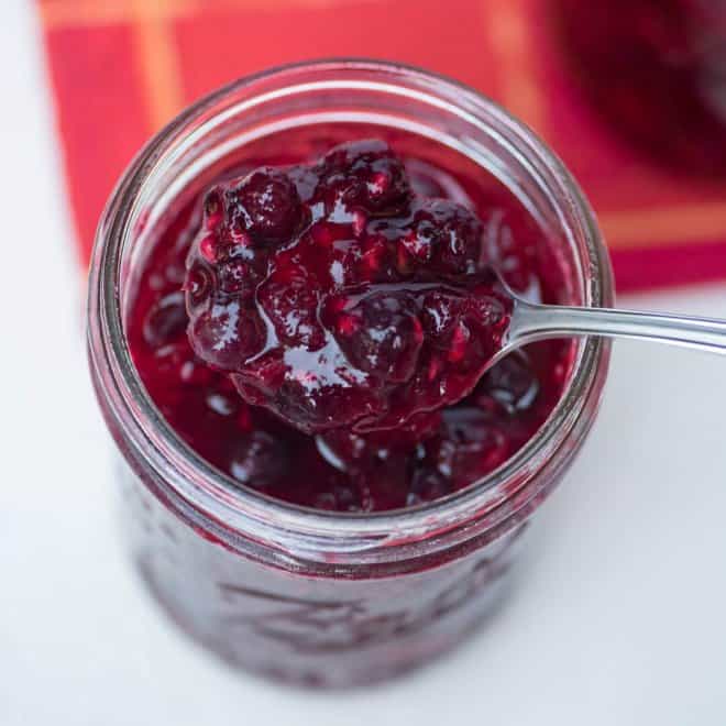 Very Berry Cranberry Sauce being lifted with a spoon out of a glass mason jar.