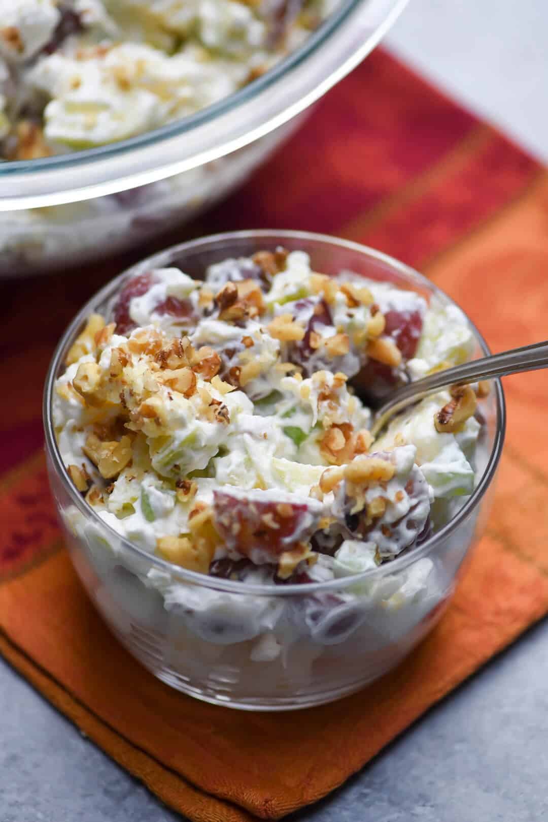 A small glass bowl full of Waldof Salad with a spoon.