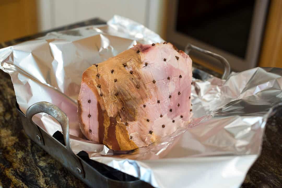 The ham with cloves in it on a sheet of foil in a roasting pan.