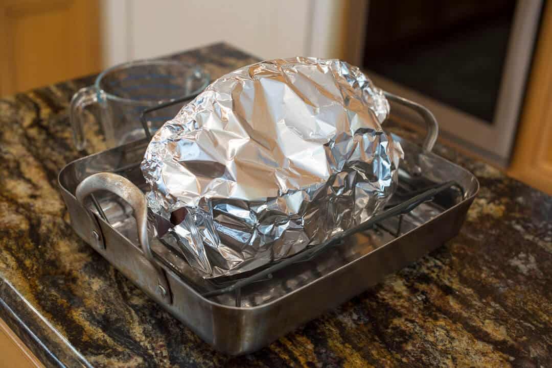 The ham enclosed in heavy duty foil on a rack in a roasting pan ready for the oven.