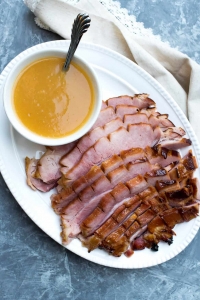 Slices of ham and a small bowl of pineapple sauce on a white platter.