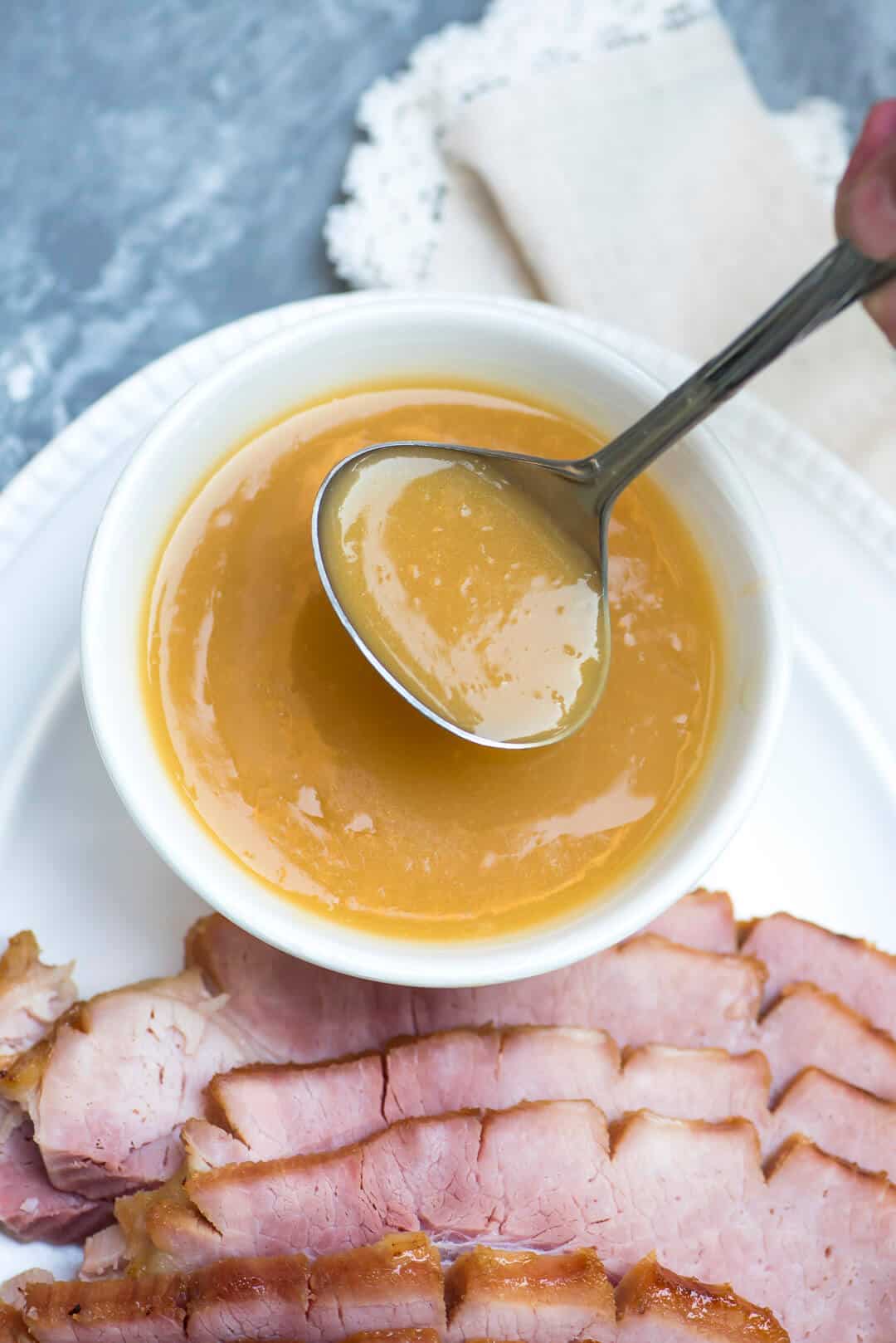 A ladle scoops pineapple sauce from a small white bowl.