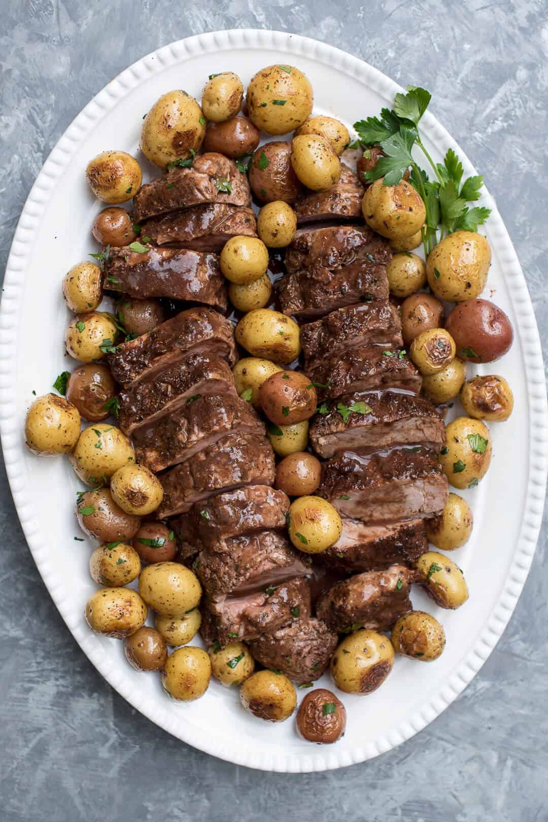 A platter with slices of pork tenderloin and potatoes.