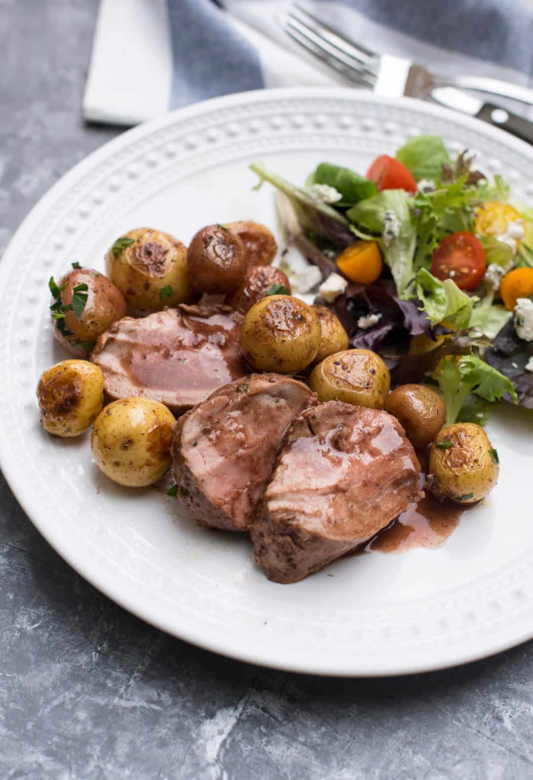 A white plate with three slices of the pork tenderloin with potatoes and a green salad.