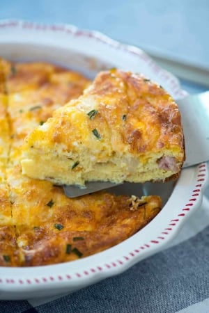 A spatula lifts a piece of crustless quiche from a pie dish.