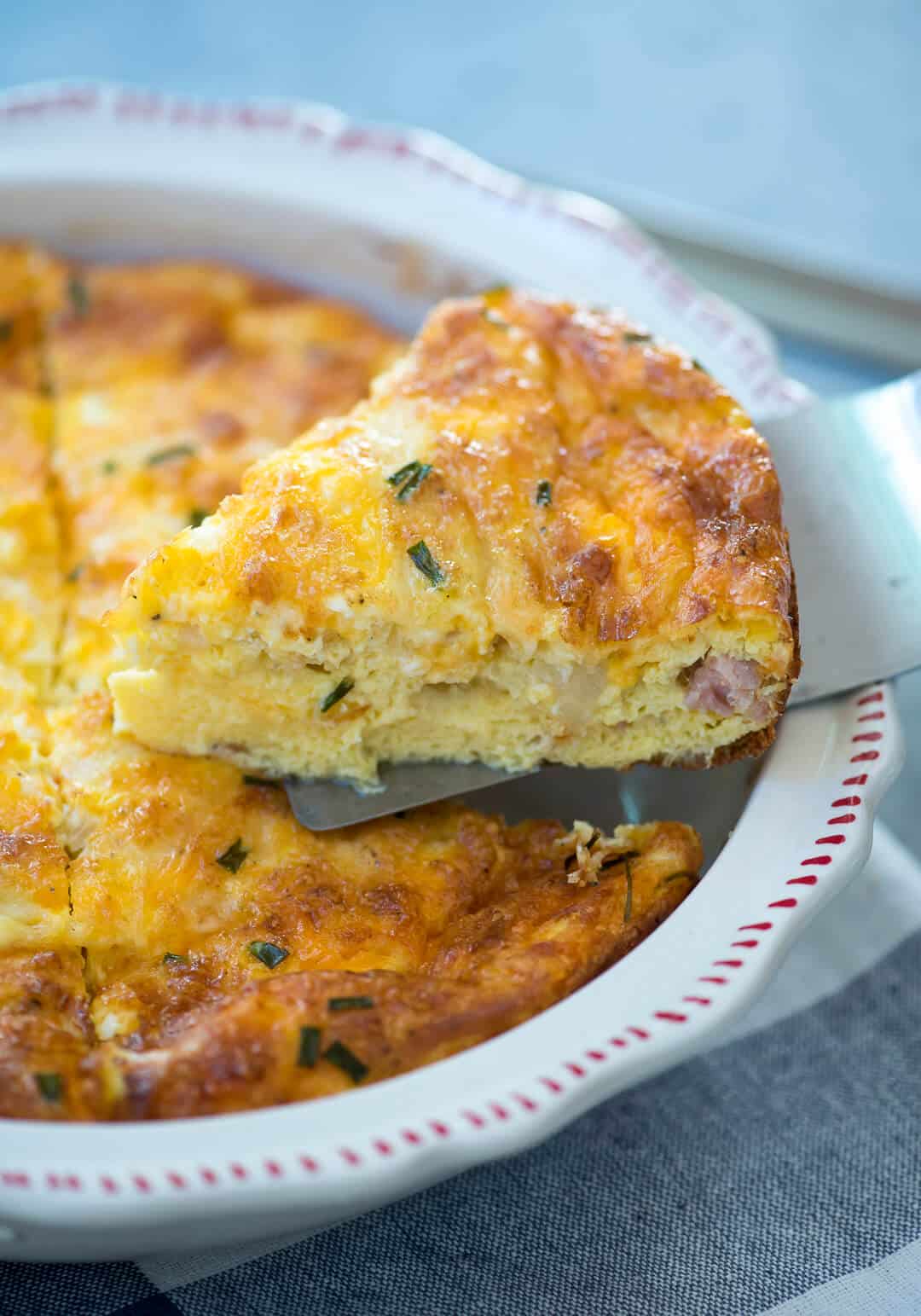 A spatula lifts a piece of crustless quiche from a pie dish.