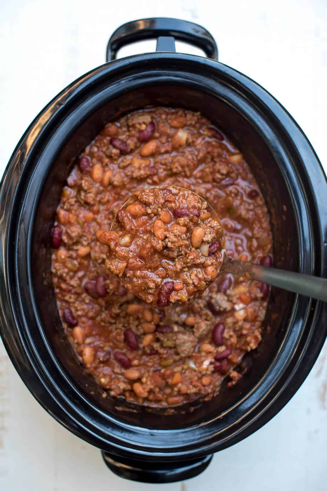 A ladle scooping up chili from a slow cooker insert.