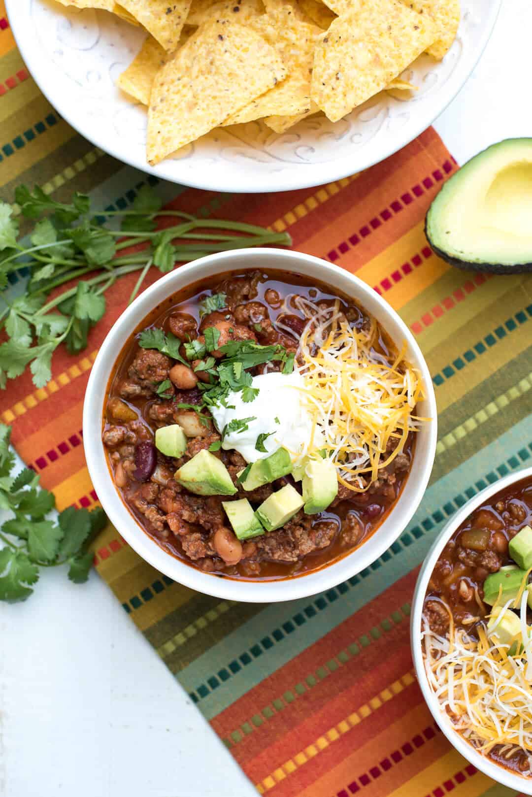 A bowl of chili with toppings on a colorful cloth.