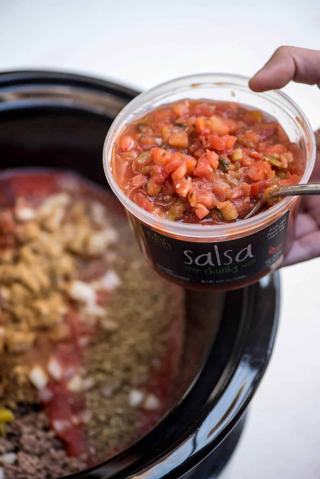 A spoon scoops the Fresh Cravings Salsa into the slow cooker.