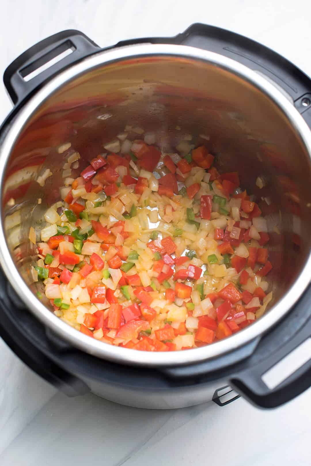 An over the top image of the onion, bell peppers and garlic cooking in the Instant Pot.