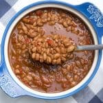 A spoon scoops up saucy beans from a blue and white bowl.