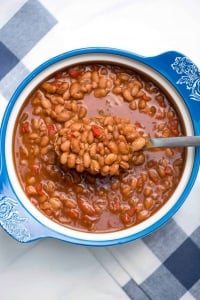 A spoon scoops up saucy beans from a blue and white bowl.