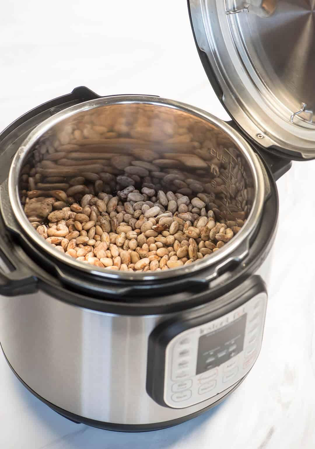 An image showing the lid resting on one of the handles of the Instant Pot revealing a pot full of dry beans.