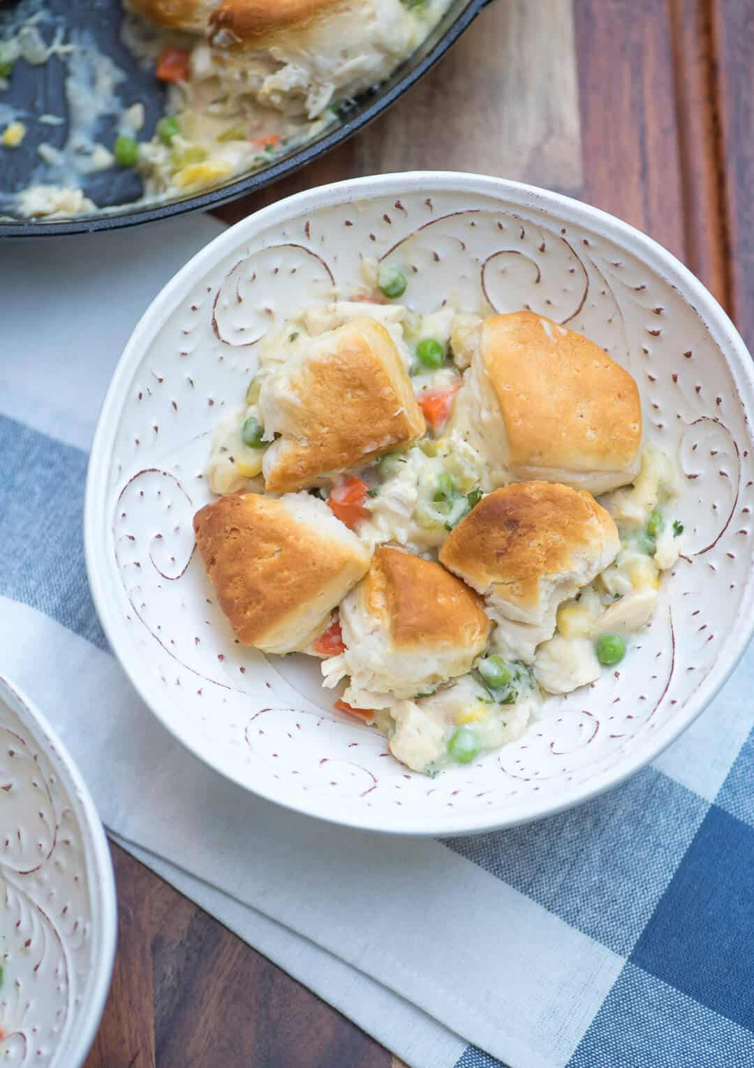  A white serving bowl filled with chicken pot pie with biscuit topping.