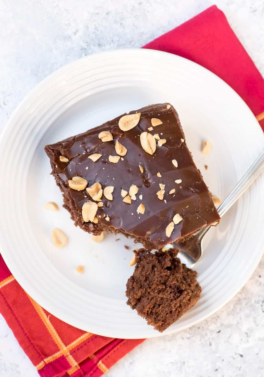 An over the top image of a slice of chocolate peanut butter cake on a white plate being broken into with a fork.