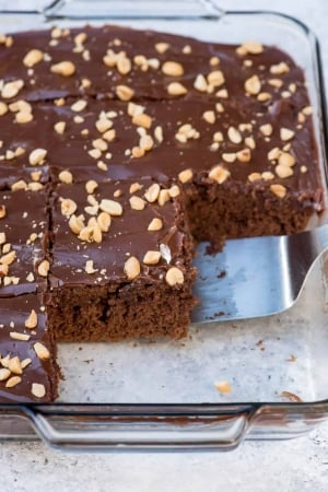 A spatula lifts a piece of chocolate cake topped with peanuts.