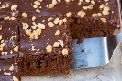 A spatula lifts a piece of chocolate cake topped with peanuts.