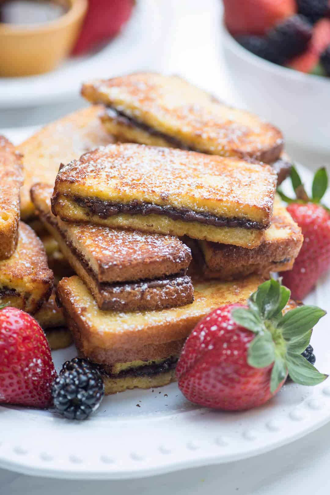 Stacks of Nutella French Toast Sticks with berries on a white plate.