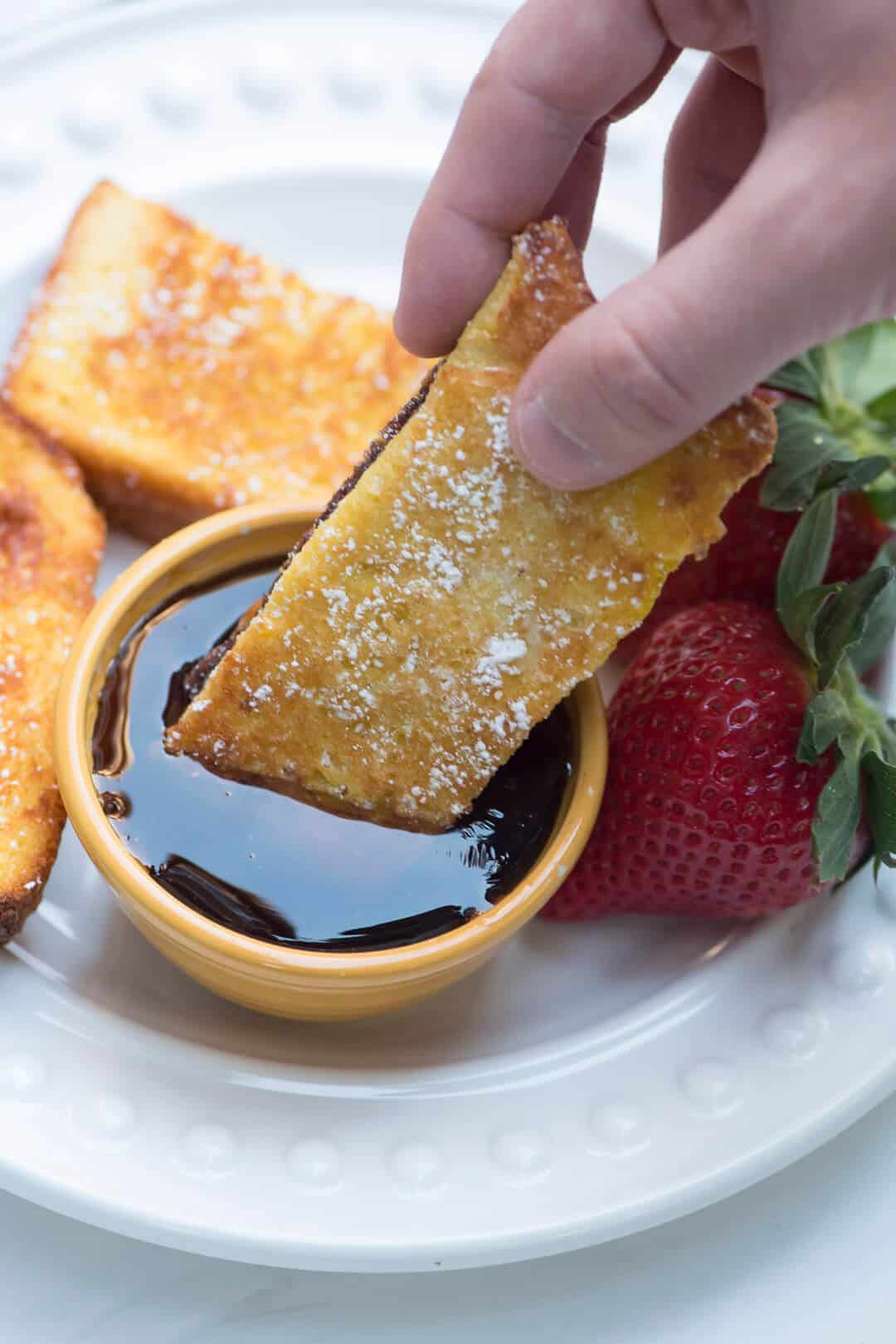 A french toast stick being dipped into maple syrup.