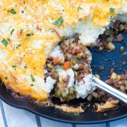 A spoon scoops up Shepherd's Pie from a skillet.