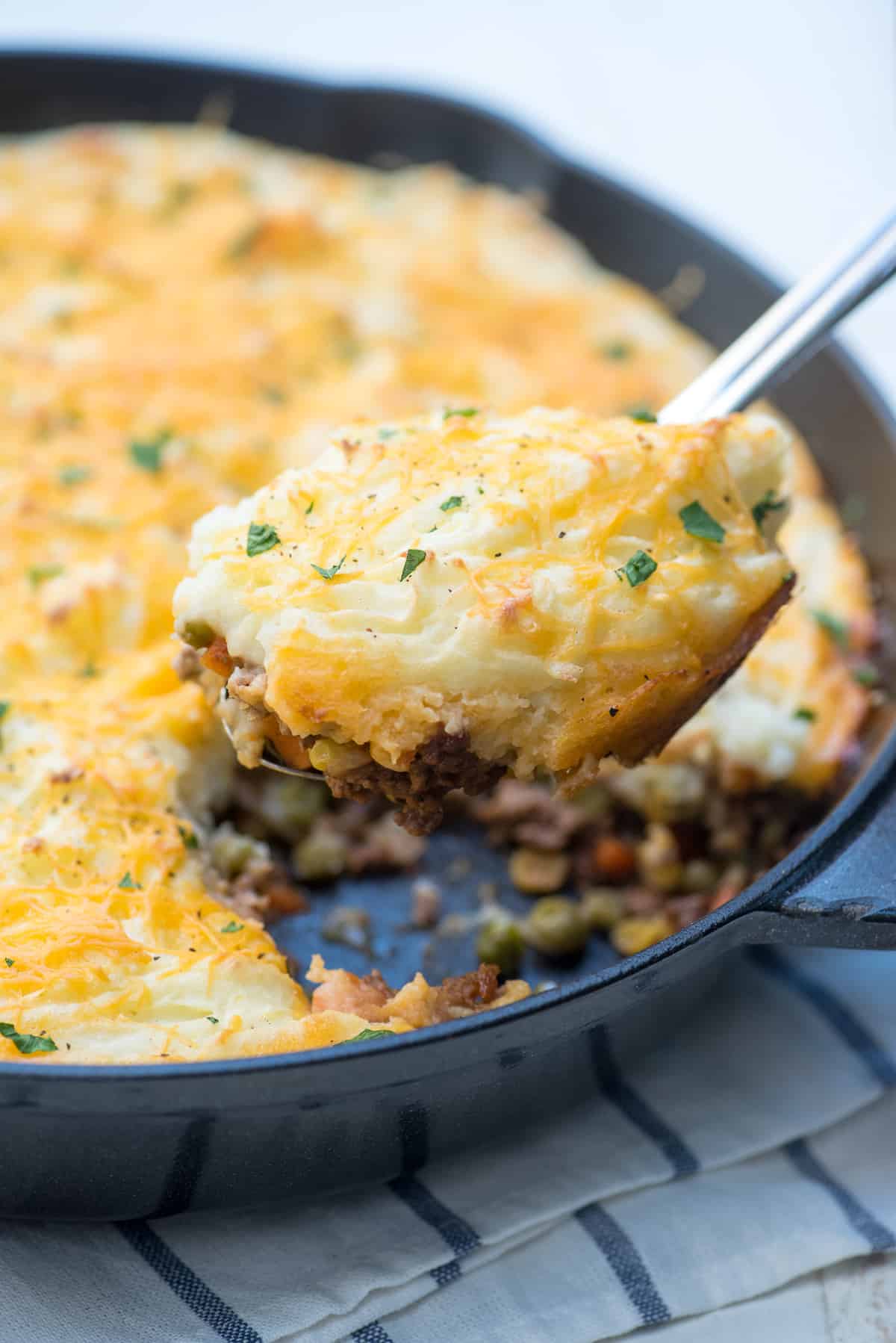 A spoon scooping shepherd's pie from a cast iron skillet.