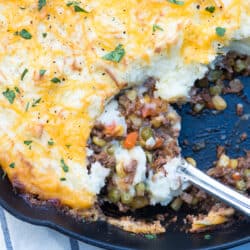 A spoon scoops up Shepherd's Pie from a skillet.