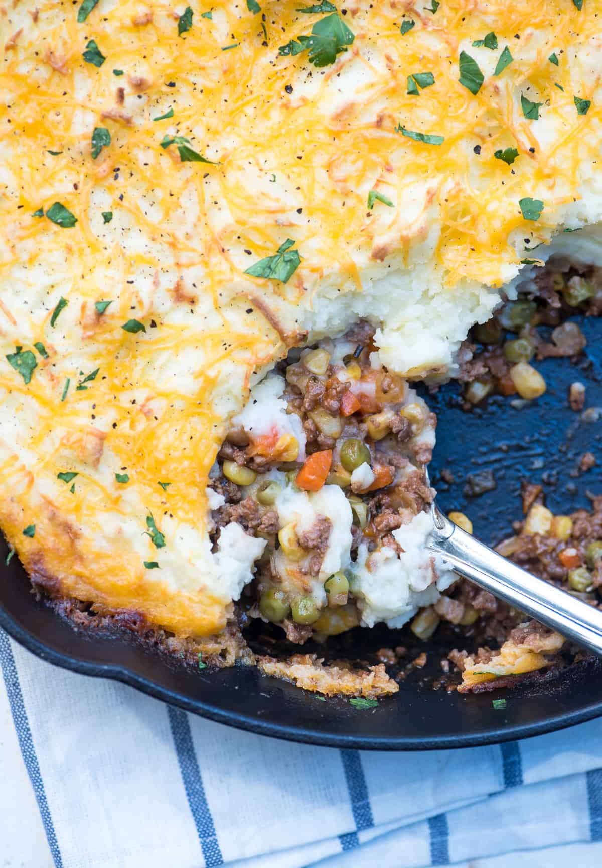 A spoon scoops up Shepherd's Pie from a skillet.