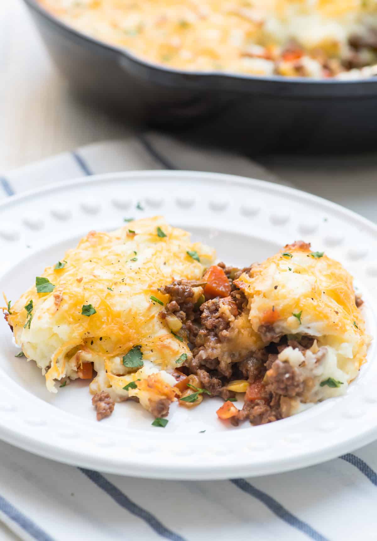 A serving of shepherd's pie with peas and carros on a white plate.