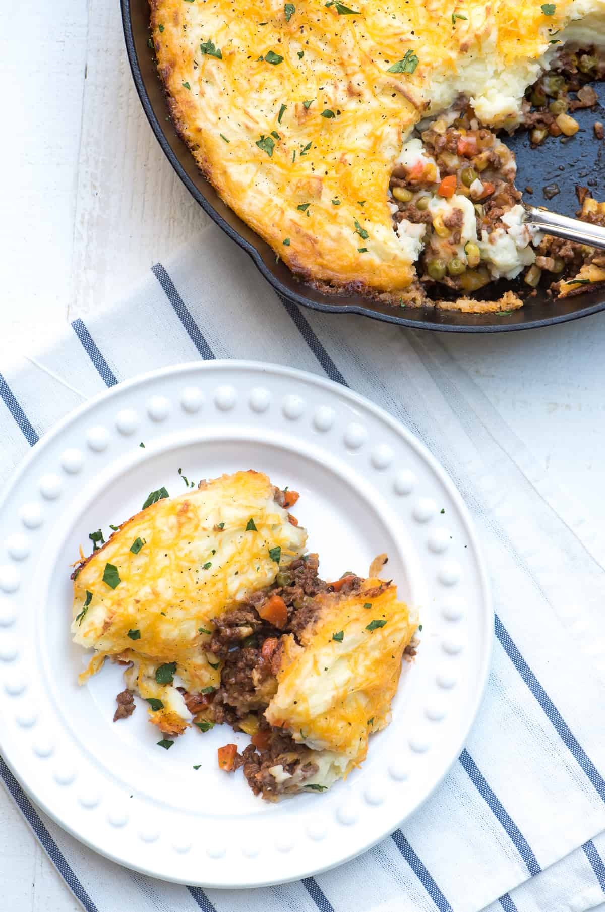 A serving of shepherd's pie on a white plate next to a cast iron skillet.