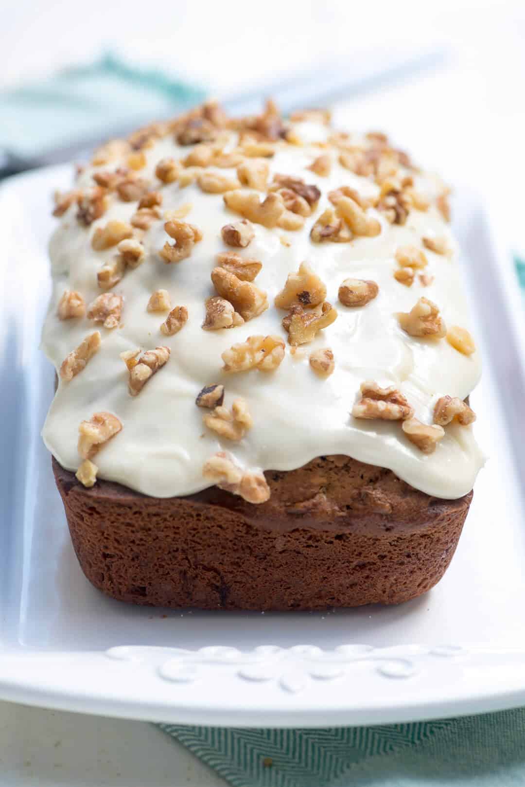 A loaf of Carrot Zucchini Bread with Cream Cheese Walnut Frosting on a white serving platter