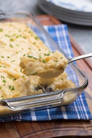 A spoon lifts mashed potatoes from a baking dish.