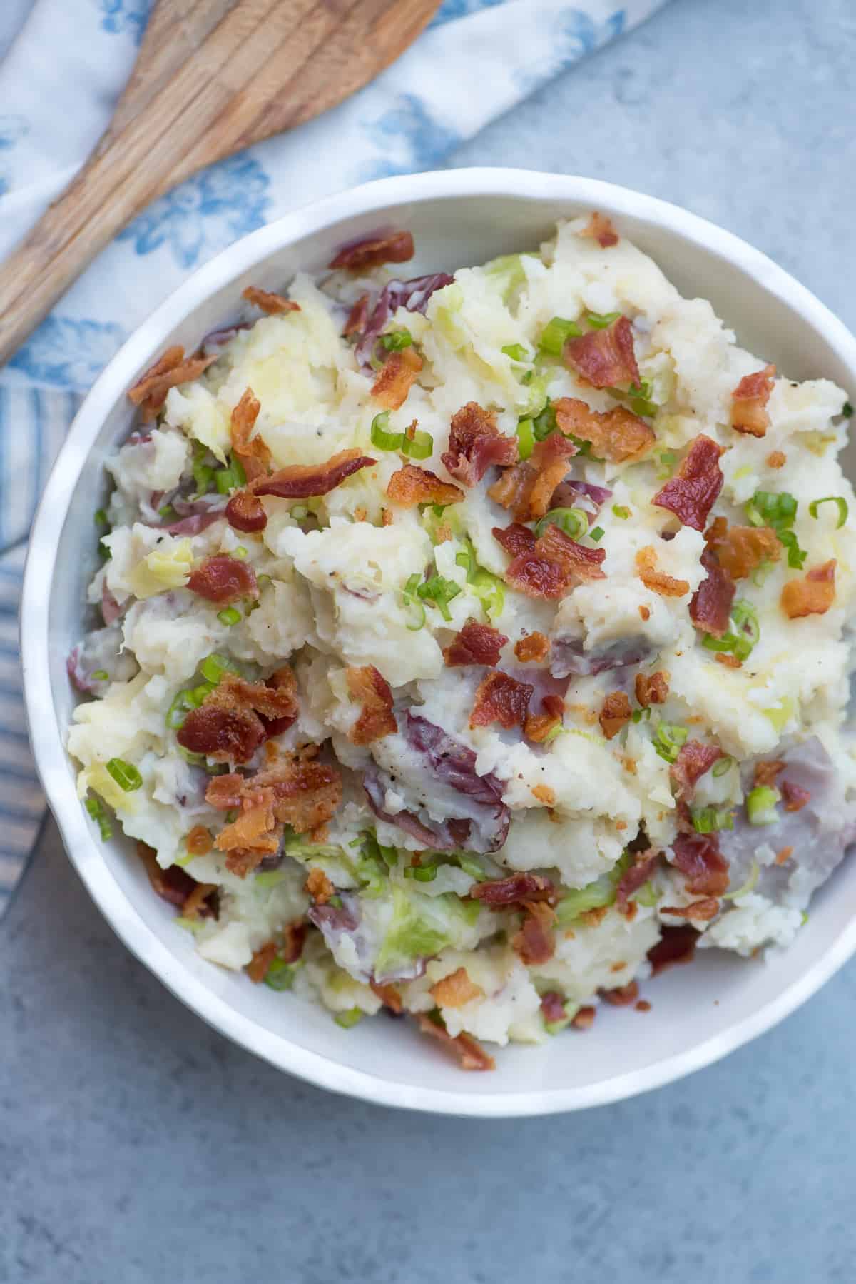 Mashed potatoes topped with bacon and green onions in a white bowl.