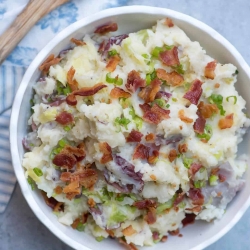Mashed potatoes topped with bacon and green onions in a white bowl.