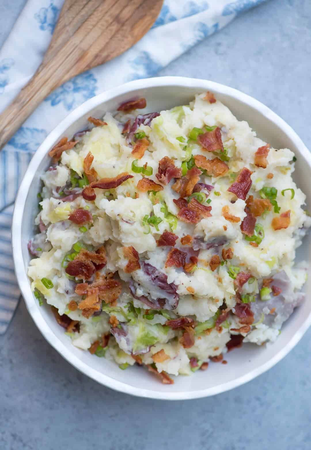 Irish Colcannon Potatoes in a white bowl with a floral blue and white cloth and wooden spoon.