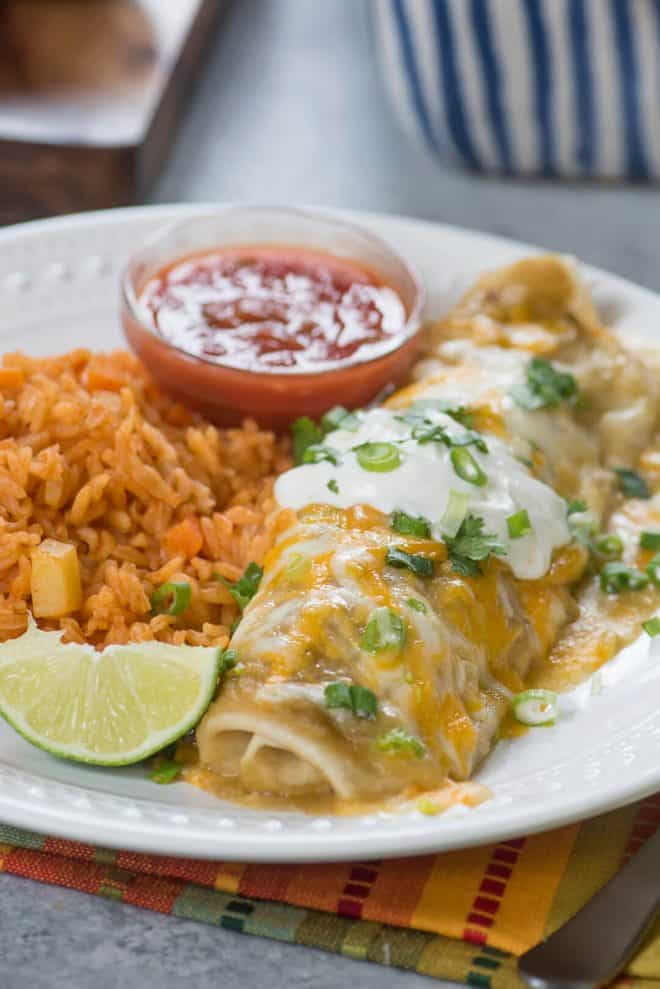 A Green Chile Chicken Smothered Burrito on a white plate with Mexican rice.