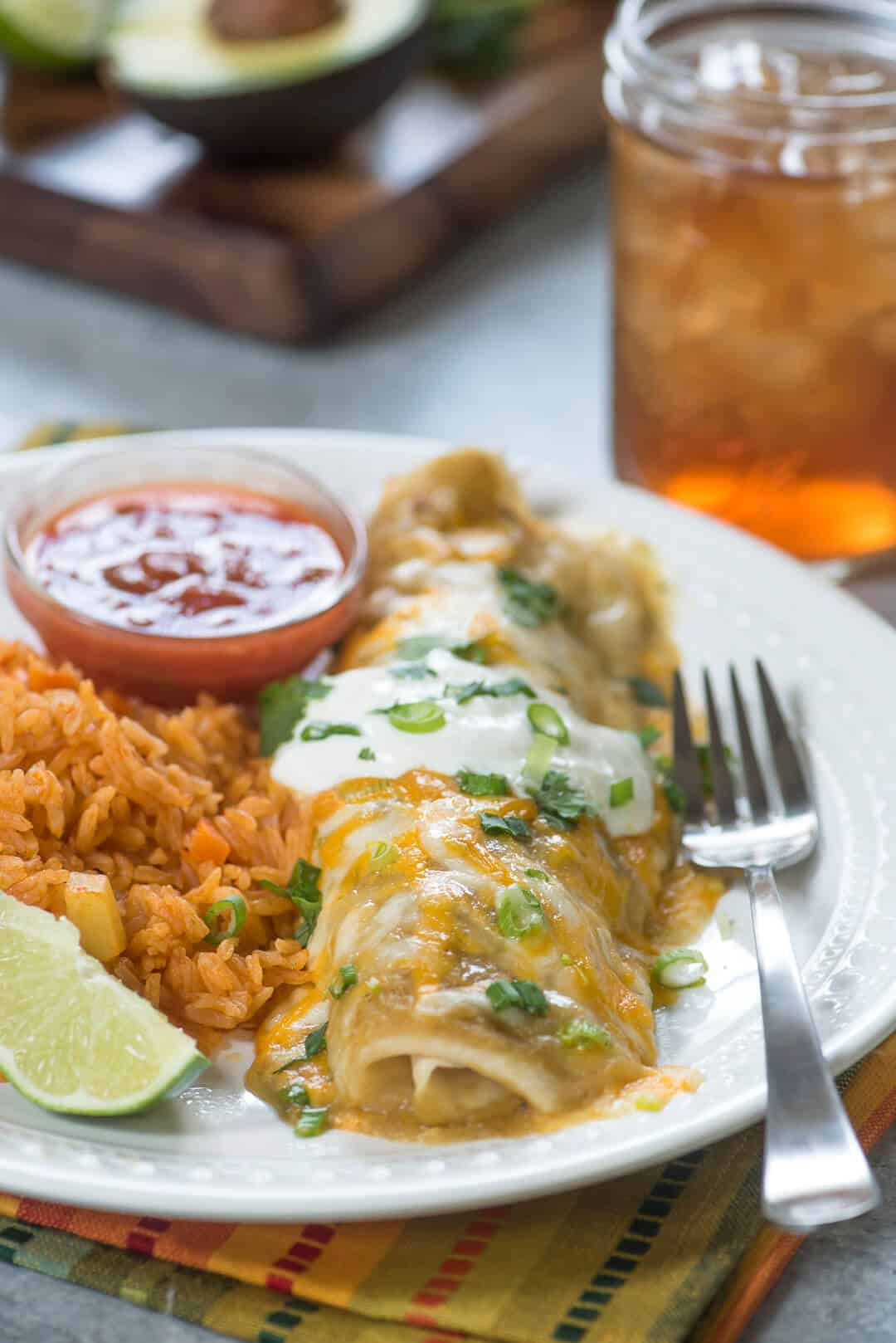 One burrito on a white plate with rice, salsa, and a lime wedge.