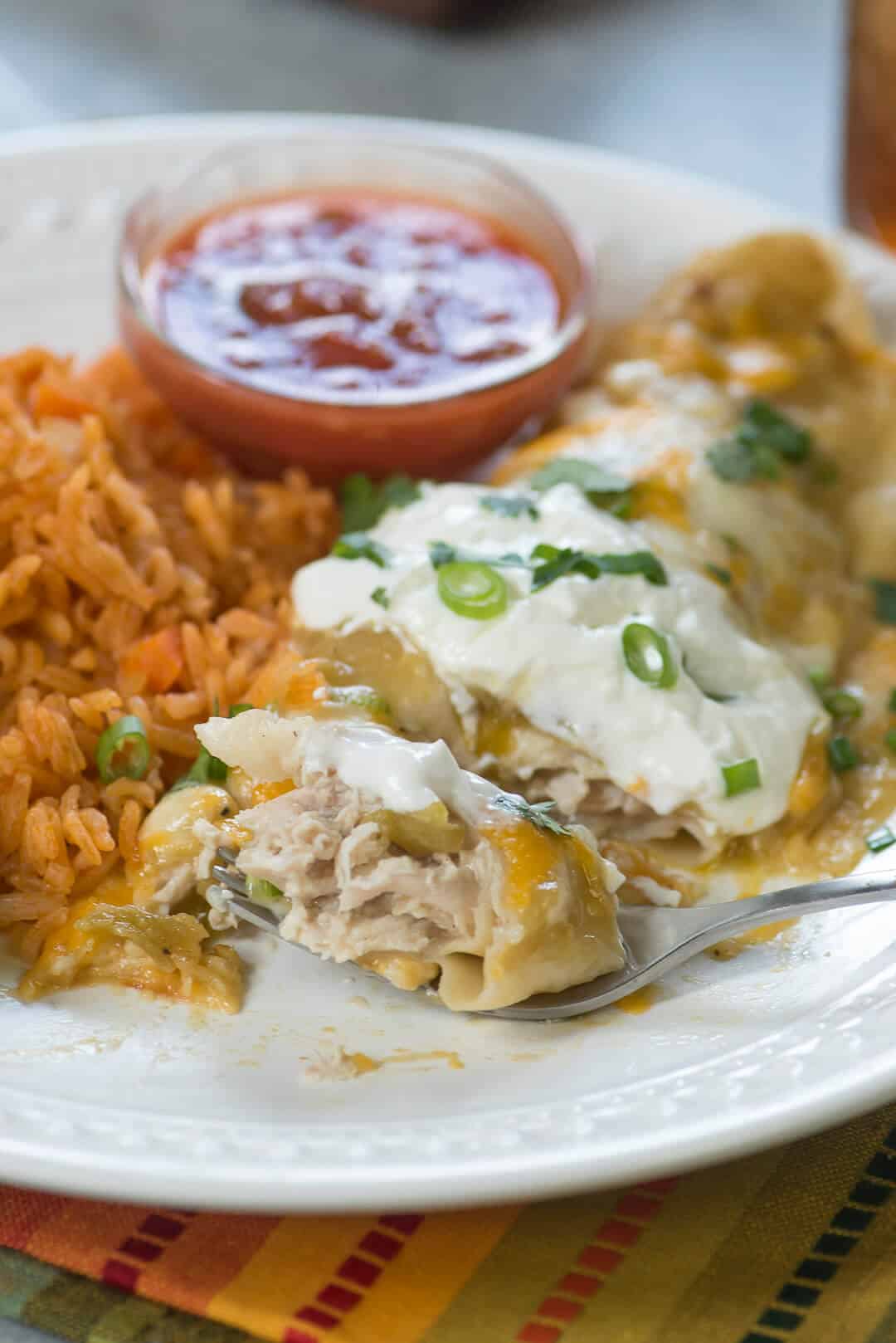 A fork breaking into a burrito on a white plate.