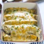 A spatula lifts a smothered burrito from a baking dish.