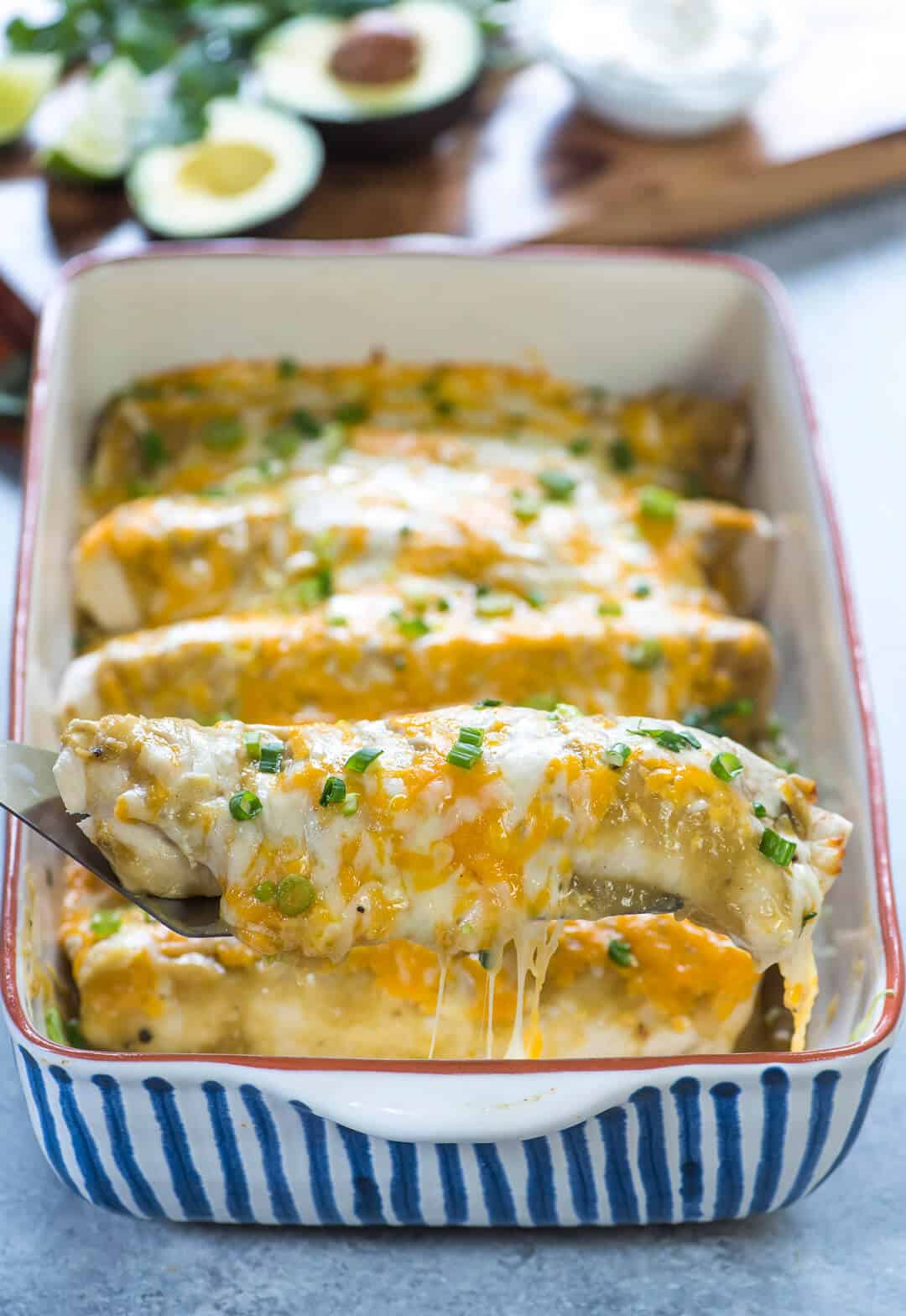 One burrito being lifted out of a casserole dish on a spatula.