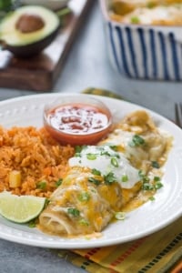 A smothered burrito topped with sour cream on a plate with rice.