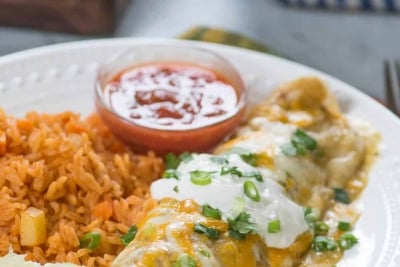 A smothered burrito topped with sour cream on a plate with rice.