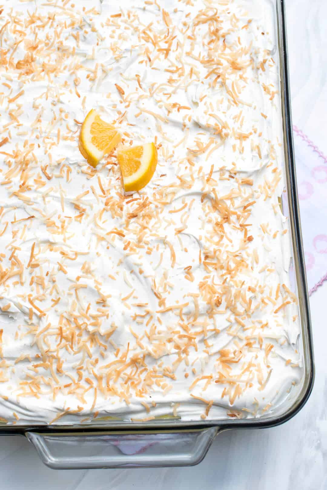 An over the top image of Lemon Coconut Poppy Seed Cake in a glass baking dish with toasted coconut and fresh lemon slices on top.