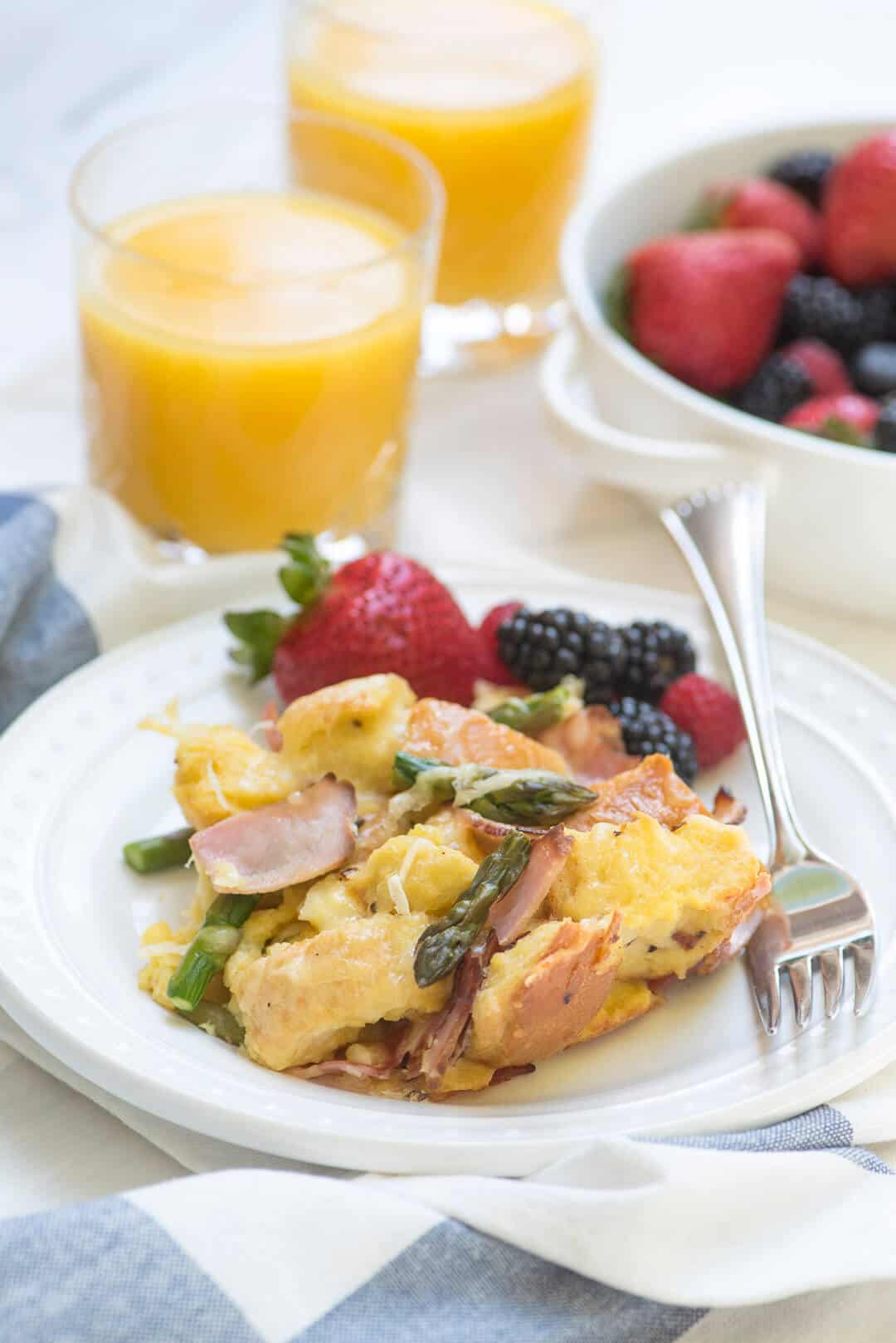  Savory French Toast Bake on a white serving plate with fresh berries and glasses of orange juice behind it.