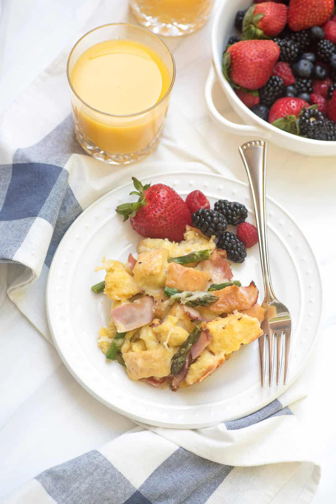 Savory French Toast Bake on a white serving plate with fresh berries with glasses of orange juice behind it.