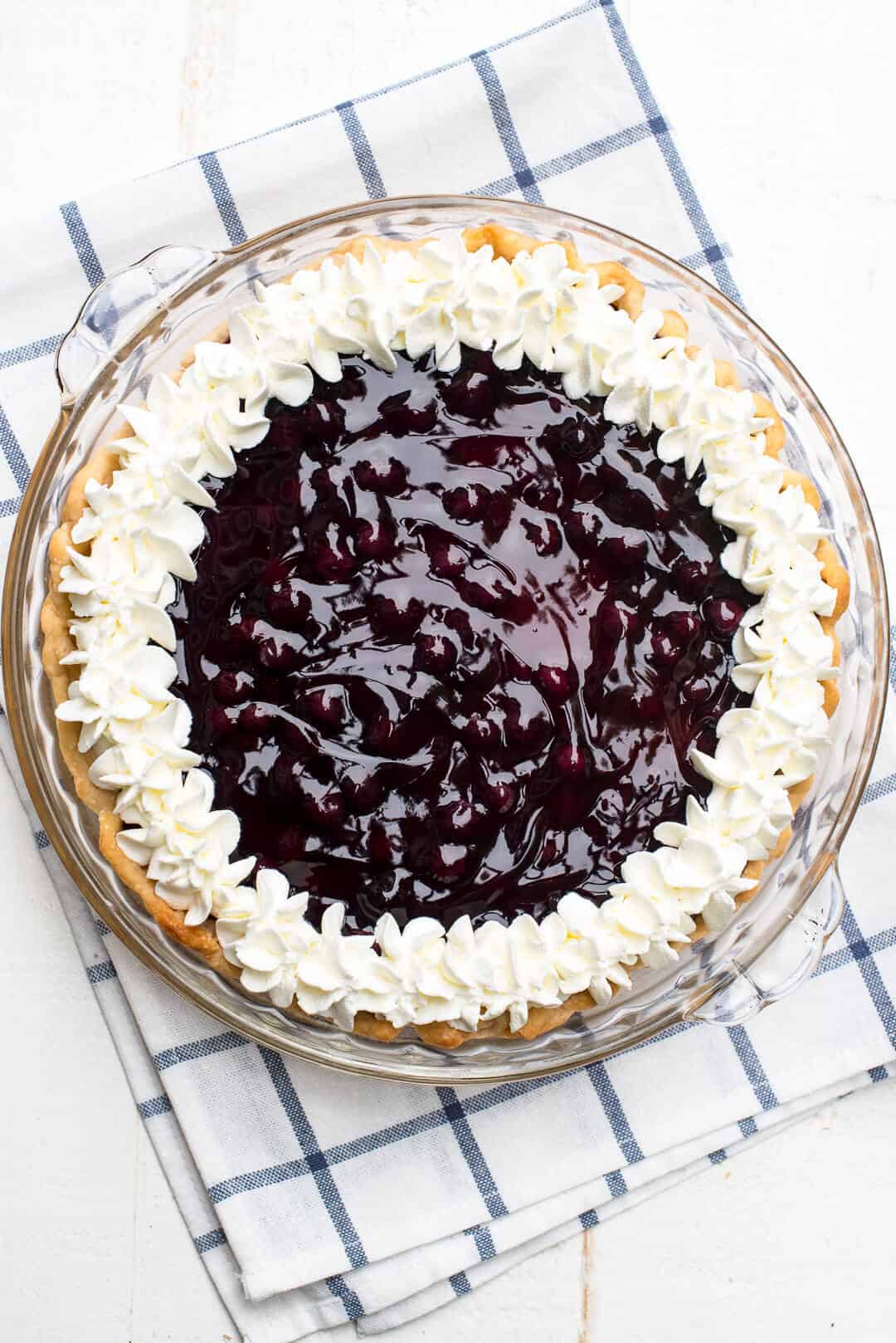 An over the top image of the Blueberry Lemon Sour Cream Pie in a pie dish placed on a blue and white striped cloth.