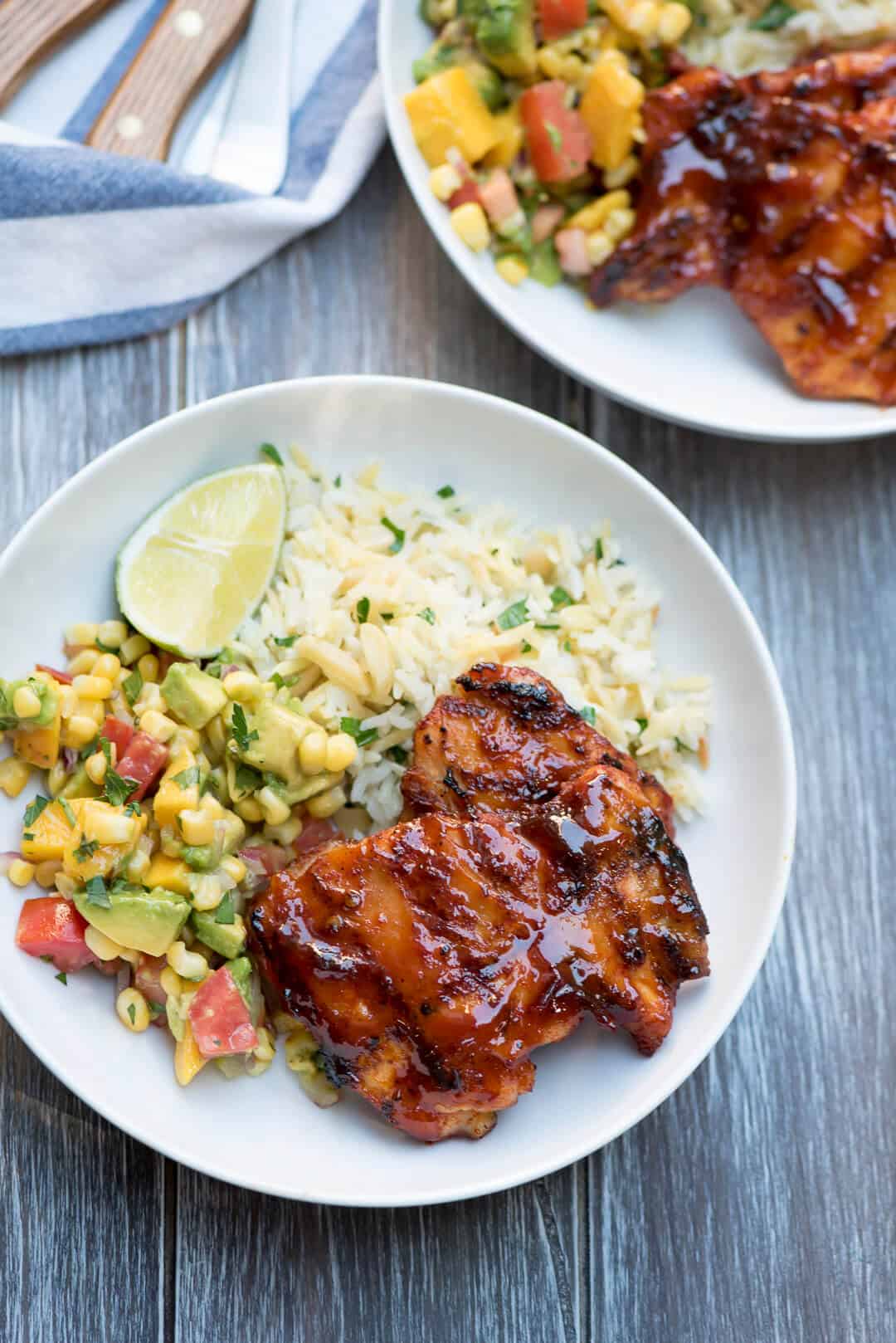 An over the top image of a white plate with grilled chicken, rice, and avocado salsa.